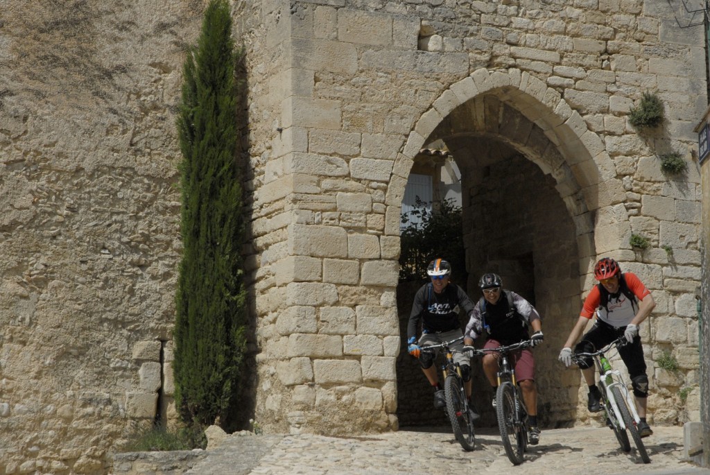 3 personnages à VTT sortant d'une rue de Saint-Saturnin-lès-Apt